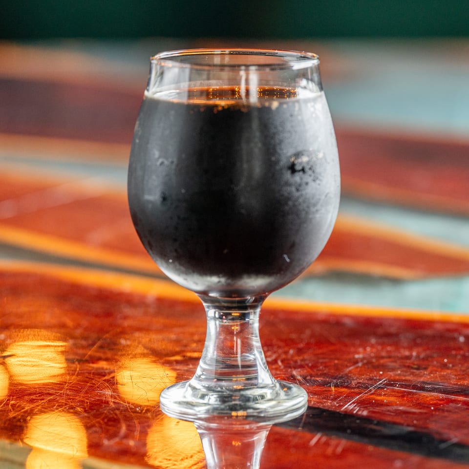 Goblet filled with a dark beverage on a glossy wooden table, reflecting colorful ambient lighting.